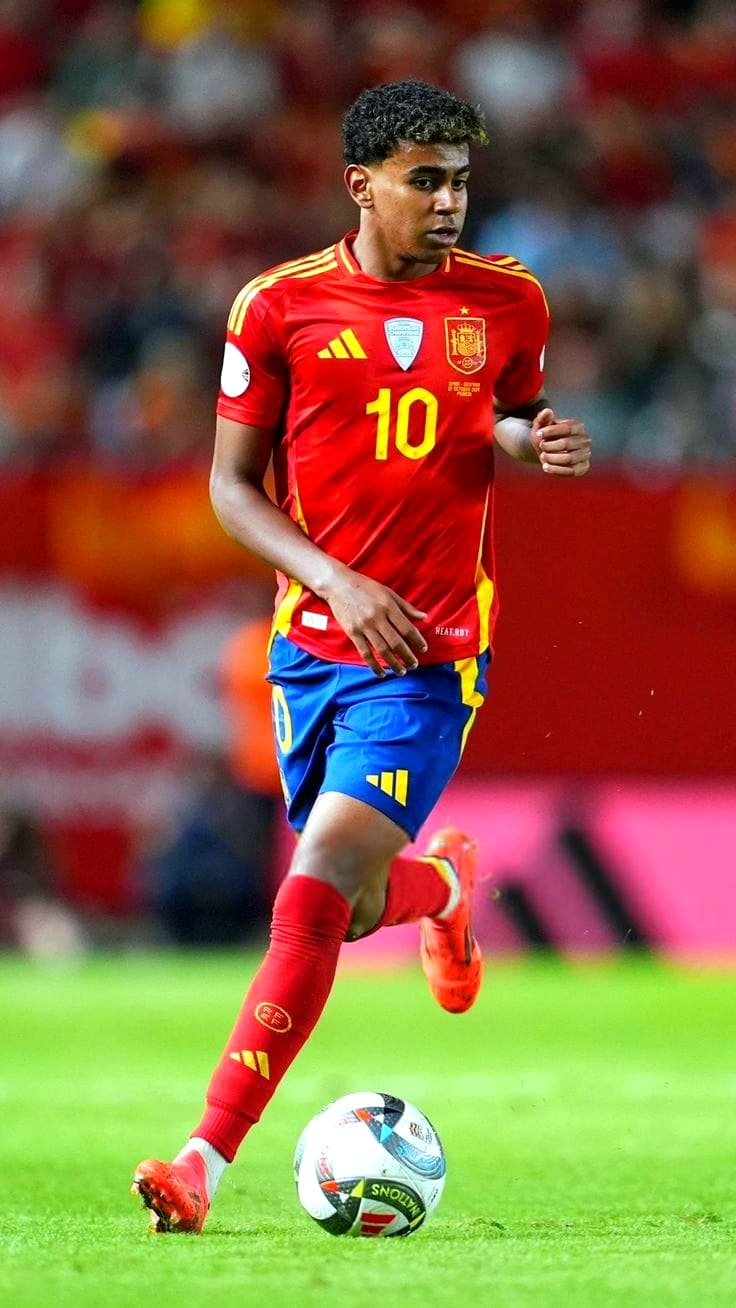 A male soccer player in a red and yellow Spain jersey with the number 10 is dribbling a soccer ball on the field during a match, streamed live via Bulgaria IPTV. The background shows a blurred crowd and stadium seats.
