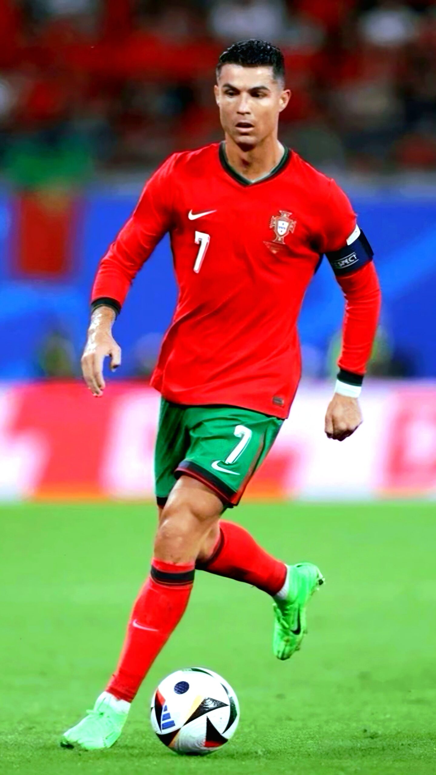 A soccer player in a red Portugal national team uniform with the number 7 dribbles a ball on the field, captured live via Bulgaria IPTV. He wears green shorts, red socks, green cleats, and a captain’s armband. The background is blurred.
