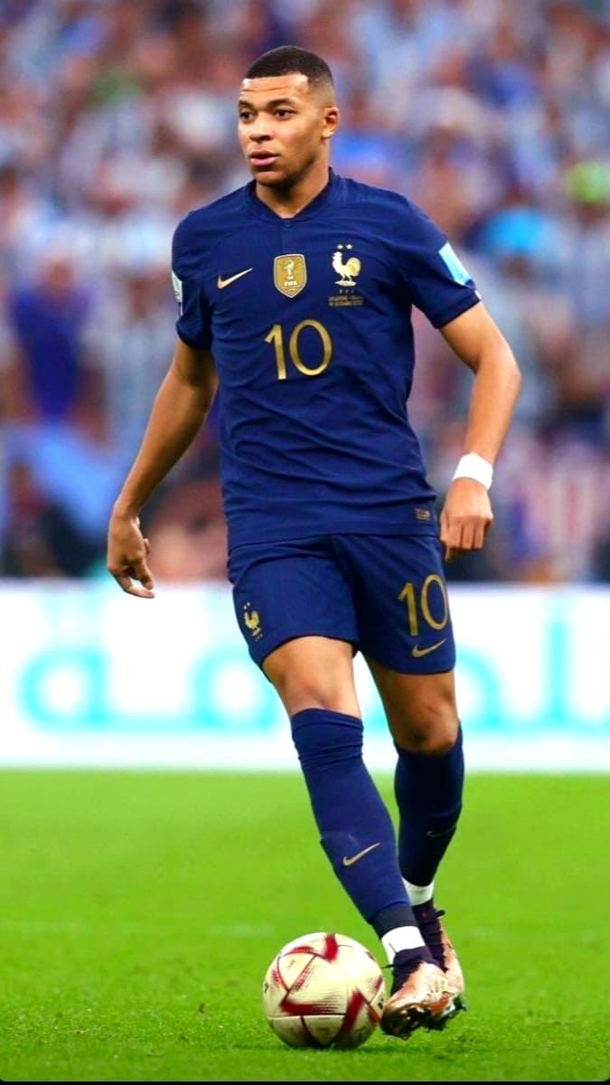 A male soccer player wearing a dark blue France national team jersey with the number 10 controls a ball on the field during a match, as fans watch in the background—stream matches live with Bulgaria IPTV.