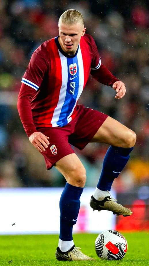 A male soccer player in a red and blue Norway national team uniform controls a soccer ball on the field during a match, as seen on Bulgaria IPTV.
