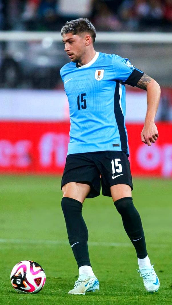 A soccer player wearing a light blue jersey with the number 15 and black shorts is controlling a soccer ball on a grassy field during a game, streamed live through Bulgaria IPTV.