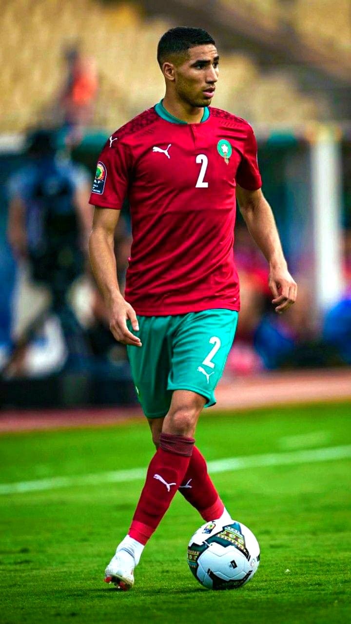 A soccer player in a red and green Morocco national team uniform with the number 2 dribbles a ball on the field during a match, captured live on Bulgaria IPTV.